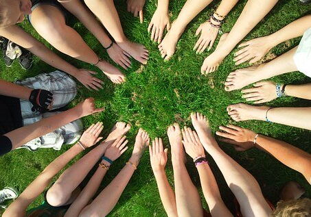 Jugendliche sitzen im Kreis und halten ihre Hände und Füße zur Mitte.